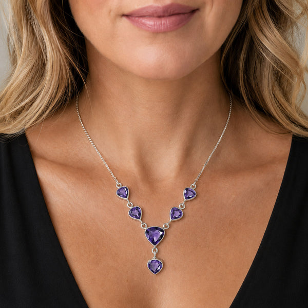 A silver necklace with a V-shaped arrangement of purple heart-shaped amethyst gemstones, worn by a model in a black top.