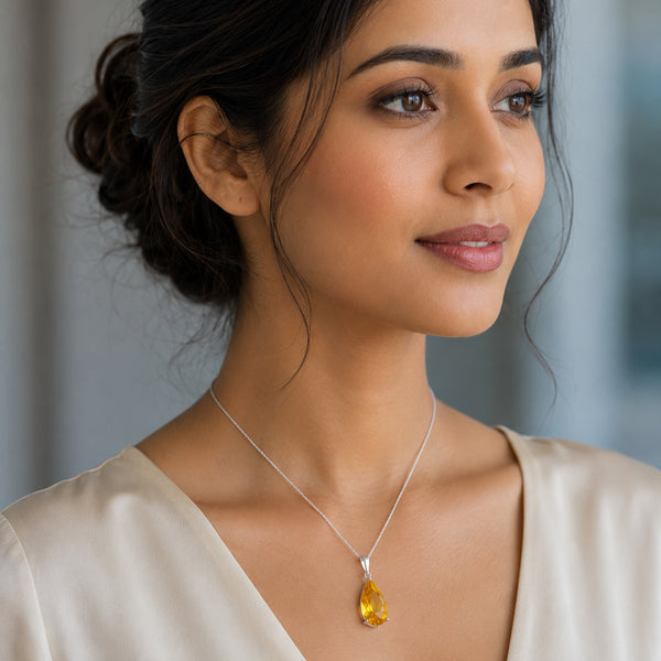 A woman wearing a silver chain necklace with a teardrop-shaped yellow citrine gemstone pendant, shown in a close-up profile view.