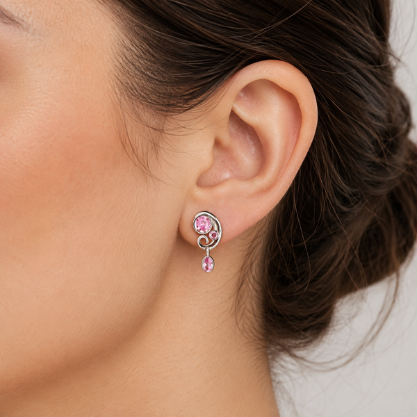 A close-up of a woman's ear wearing a silver-toned spiral drop earring with pink gemstones.